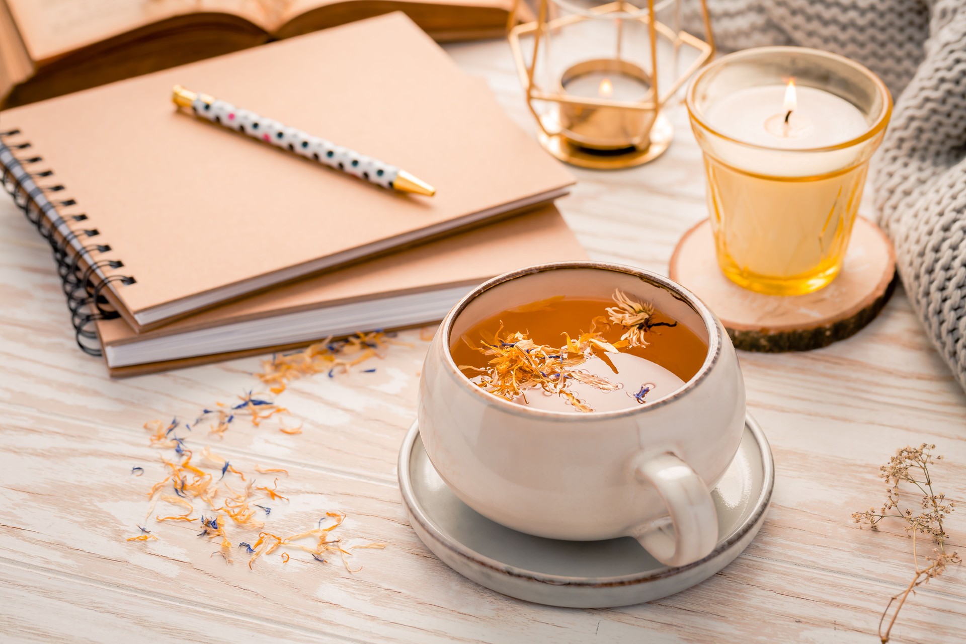 Hot herbal tea with notepad, candle, book and blanket
